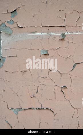 Vertikale Nahaufnahme einer gealterten, hellbraun gestrichenen Wandoberfläche mit abblätternder, rissiger und abplatzender Farbe Stockfoto