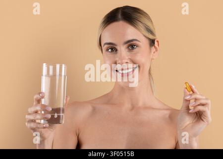 Junge Frau lächelt, während sie ein Glas Wasser und eine Softgel-Kapsel hält Stockfoto
