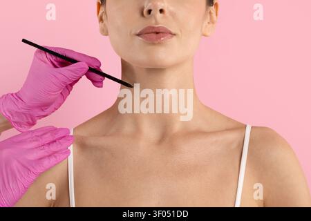 Behandschuhte Hand hält einen Bleistift in der Nähe des Halses einer jungen Frau und bereitet sich darauf vor, den Bereich zu markieren Stockfoto