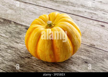 Leuchtend gelber Kürbis mit gerippter Textur auf verwittertem grauem Holz. Sanfte natürliche Beleuchtung hebt herbstliche Töne und organische Formen hervor. Ideal für Stockfoto