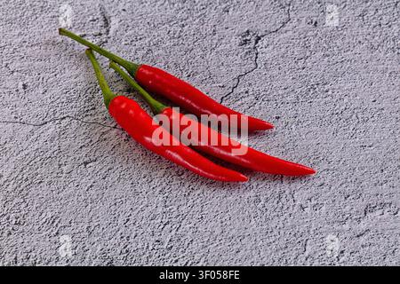 Leuchtend rote Chilischoten mit grünen Stängeln, die diagonal auf rauem grauen Betonhintergrund angeordnet sind. Natürliches Licht hebt die glänzende Oberfläche der Pfefferhaut hervor Stockfoto