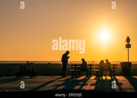 Silhouetten von Menschen, die während des Sonnenuntergangs auf Bänken auf dem Radweg entlang des Pazifischen Ozeans in Südkalifornien entspannen Stockfoto