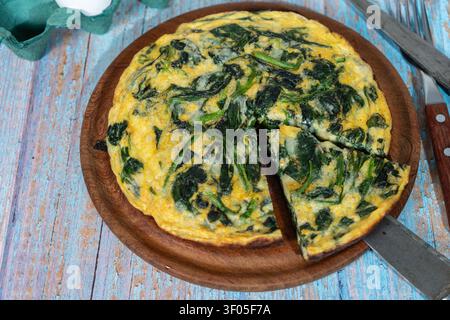 Runde Spinatfrittata oder Omelett auf einem Teller mit Besteck auf einer rot-weißen karierten Serviette. Gesunde Hausmannskost Stockfoto