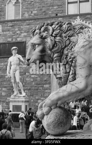 Nahaufnahme einer Medici-Löwen-Statue an der Loggia dei Lanzi mit einer Nachbildung von Michelangelos David im Hintergrund, Florenz, Italien. Stockfoto