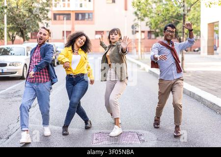Energetische, vielfältige Freunde tanzen verspielt auf einer ruhigen Stadtstraße. Multiethnische Millennials und Gen Z zeigen unbeschwerte Freude und Bewegung im Freien. Urban y Stockfoto