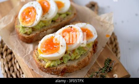 Zwei Scheiben knuspriger Sauerteig mit cremigem Avocado-Brei und marmelierten weichen gekochten Eiern. Die Szene bietet helles natürliches Licht und rustikale Textur Stockfoto