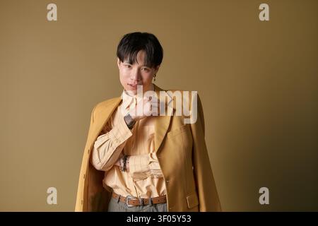 Ein junger Mann in stilvoller Kleidung posiert selbstbewusst mit einem charmanten Lächeln vor einem warmen Hintergrund. Stockfoto