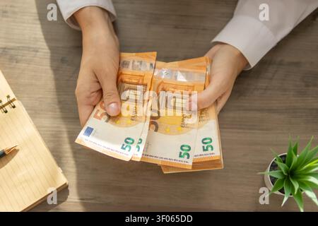 Hände, die zahlreiche Bündel von 50-Euro-Banknoten auf einem hölzernen Schreibtisch halten und auffächern, die Finanztransaktionen, Cashflow und Geschäftseinnahmen darstellen Stockfoto