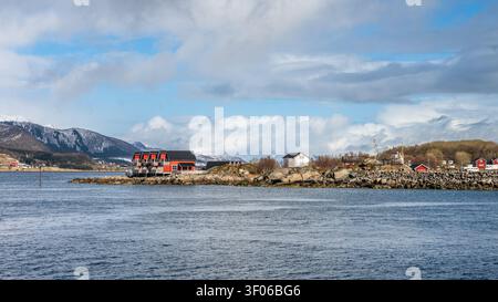 Typische rote Holzhäuser auf einer Insel in der Nähe von Hammerfest in Norwegen an einem klaren Tag mit blauem Himmel, vom Wasser aus gesehen Stockfoto