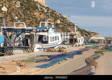 Im Hafen von Calpe, Spanien, legten Fischerboote an, mit bunten Netzen, die am Kai trocknen, Seilen und Winden im Vordergrund und felsigen Klippen Stockfoto