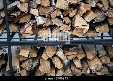 Ordentlich gestapeltes Brennholz in einem stabilen Metallgestell mit natürlichen Holzstämmen. Perfekte Darstellung nachhaltiger, erneuerbarer Energiequellen für Stockfoto