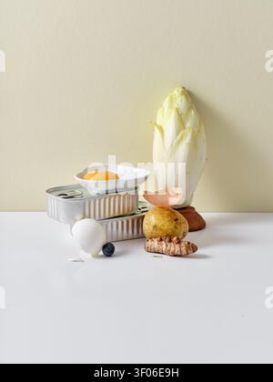 Eine kreative Stillleben-Komposition mit Zutaten wie Kartoffeln, Eigelb in einem Gericht, Fisch aus der Dose, Zichorien, Kurkuma und Heidelbeere Stockfoto