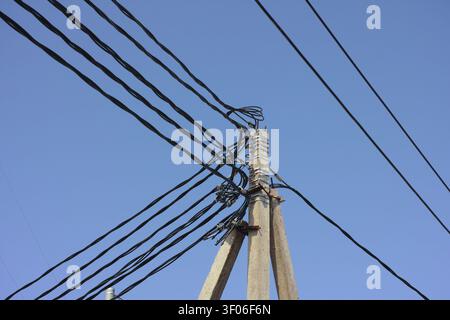 Niedrigwinkelaufnahme eines Betonmasts mit einem komplexen Verwirr schwarzer Stromleitungen vor klarem blauem Himmel. Stockfoto