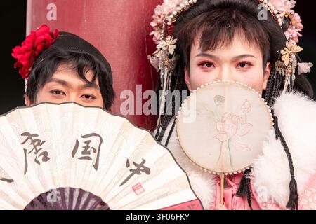 Zwei junge Männer in traditionellem Hanfu posieren in der Nähe der Xi'an Stadtmauer in China, halten dekorative Handfächer und tragen kunstvolle Haaraccessoires und fangen cla ein Stockfoto
