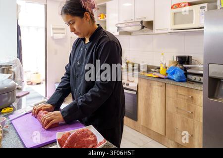 Frauenköchin bereitet rohes Rindfleisch auf einem Schneidebrett in einer Küchenstube zu Stockfoto