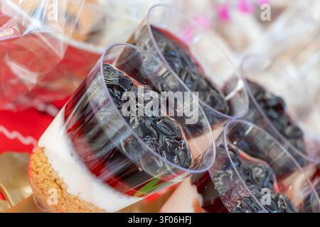 Nahaufnahme von geschichteten Kirschdessertbechern mit Biskuitboden, Sahne und dunkler Beerenoberseite, angeordnet auf einer festlichen Catering-Auslage mit weicher Fokussierung und co Stockfoto