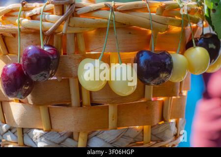 Nahaufnahme von frischen roten und gelben Kirschen, die aus einem rustikalen Weidenkorb hängen und eine authentische Sommerfruchtauslage auf einem traditionellen Markt bilden Stockfoto