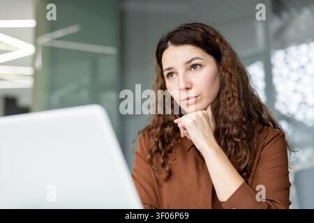 Frau, die sich auf Daten in einer professionellen Büroumgebung konzentriert und analysiert, über Herausforderungen und Möglichkeiten nachdenkt, während sie an ihrem Laptop arbeitet Stockfoto