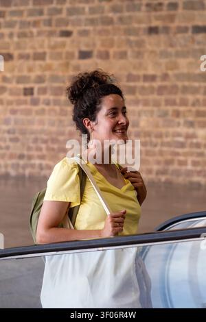 Lächelnde junge Frau fährt auf der Rolltreppe in der Station Stockfoto