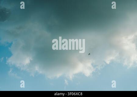Kleines Flugzeug fliegt über einen Himmel voller dramatischer Wolken und blauer Flecken. Minimalistische Flugszene mit weitläufiger Atmosphäre Stockfoto