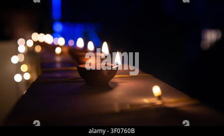 Eine Reihe von beleuchteten Ton-Diyas, die während einer Nachtfeier hell brennen, mit weichen blauen und goldenen Bokeh-Feuerlichtern, die den dunklen Hintergrund beleuchten Stockfoto