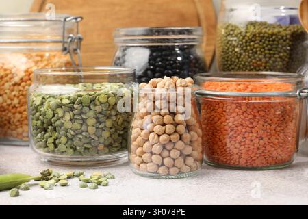 Verschiedene Arten von Hülsenfrüchten in Glasgläsern auf grauem Tisch, Nahaufnahme Stockfoto