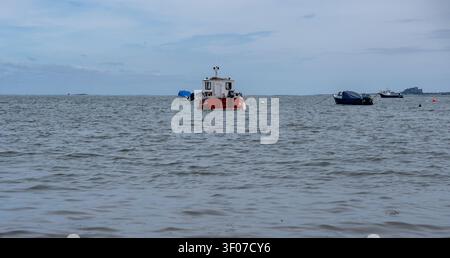 Boote, die auf dem rauen Wasser vor Holy Island an der Küste von Northumberland liegen, schaukeln gegen die Wellen unter einer dramatischen, windgekräuselten See. Stockfoto