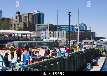 Menschen entspannen in bunten Stühlen entlang der belebten Uferpromenade von Halifax an einem klaren, sonnigen Frühlingstag. Stockfoto