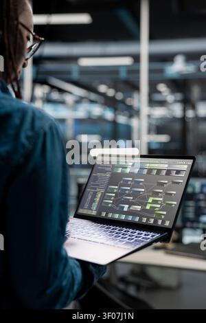 Ein Rechenzentrumsadministrator verwendet einen Laptop, um Neuronennetz-Konfigurationen zu untersuchen, und arbeitet mit KI-Technologie und Hochleistungssystemen. Stockfoto