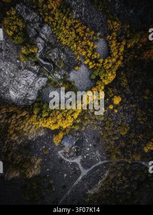 Blick aus der Vogelperspektive auf ein Haus, eingebettet zwischen lebhaften Herbstbäumen und felsigem Gelände mit einem kleinen Bach in Bishop, Kalifornien, USA. Stockfoto