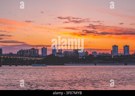 Stadtbild von Wolgograd bei Sonnenuntergang über der Wolga in Russland. Schöne urbane Landschaft mit Brücke, Wohnhäusern und farbenfrohem Orange und Stockfoto
