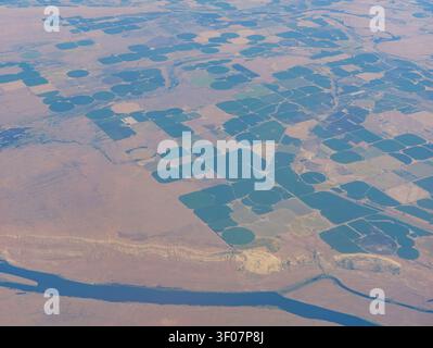 Hochwinkelansicht von landwirtschaftlich genutztem Land mit kreisförmigen grünen Feldern und einem Fluss im Vordergrund. Stockfoto
