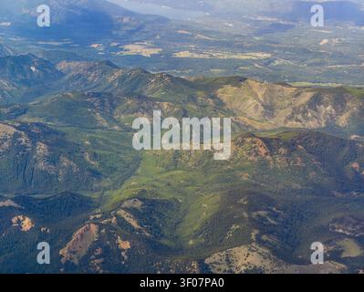 Aus der Vogelperspektive auf sanfte grüne Bergkämme und Täler, die von dichten Nadelwäldern mit Flecken freiliegender Erde bedeckt sind. Stockfoto
