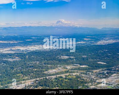Aus der Vogelperspektive eine weitläufige Vorstadtlandschaft mit dichten Wäldern und Autobahnen, die zum schneebedeckten Gipfel des Mount Rainier im di führen Stockfoto