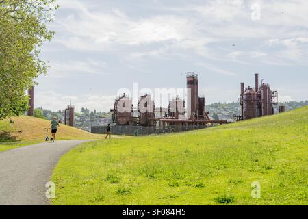 Washington State, JUN 21, 2026 - Verlassene verrostete Industriegebäude und Schornsteine stehen auf einem grasbewachsenen Hügel neben einem gepflasterten Wanderweg mit Stockfoto