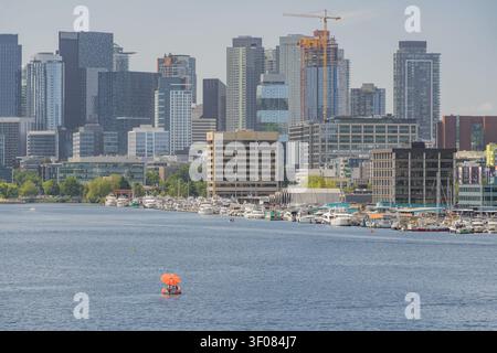 Washington Staat, Vereinigte Staaten, 21. JUN 2026 - Eine Ansicht der Seattler Stadt Skyline und des Yachthafens mit festgemachten Booten, mit einem kleinen orangefarbenen Parasail Stockfoto