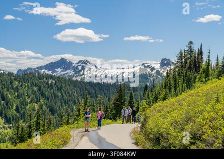 Washington State, USA, 22. Juni 2026 - Gruppe von Wanderern, die auf einem gepflasterten Pfad in einem Nationalpark mit immergrünen Wäldern und schneebedeckten Pfaden spazieren Stockfoto