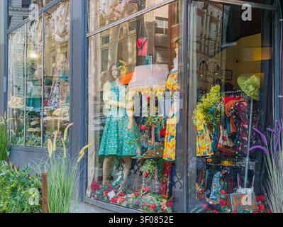 Washington State, USA, 20. Juni 2026 - Ein farbenfroher Schaufenster zeigt eine Schaufensterpuppe in einem grünen gemusterten Kleid, umgeben von Kunstwerken Stockfoto