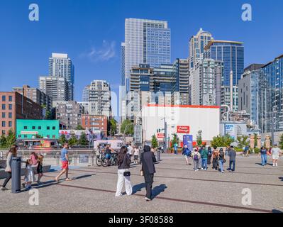 Washington State, USA, 21. Juni 2026 - Fußgänger spazieren über eine gepflasterte plaza in Seattle, Washington, mit modernen Wolkenkratzern und einer öffentlichen S Stockfoto