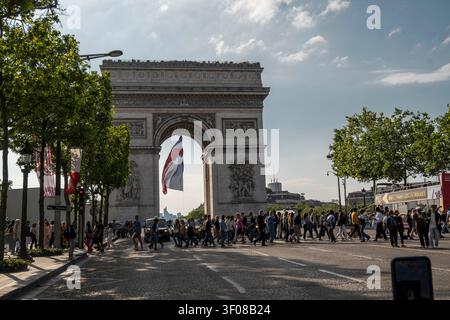 Paris, Frankreich – 6. Juni 2024: Ein weiter Blick auf den historischen Arc de Triomphe in Paris mit einer großen französischen Flagge, die im Inneren hängt. Menschenmengen von Fußgängern überqueren Stockfoto