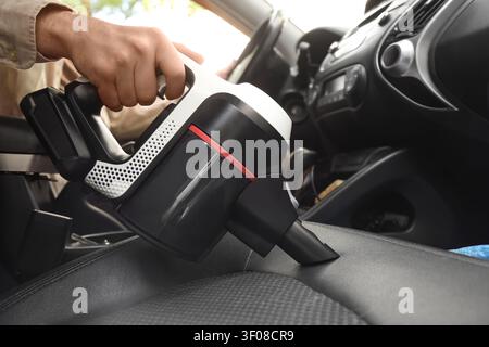 Person, die den Autositz mit einem Handstaubsauger reinigt Stockfoto