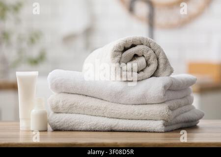 Stapel sauberer Handtücher mit Hautpflegeflaschen auf Holzoberfläche Stockfoto