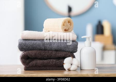 Stapel Handtücher mit Luffa und Lotionflasche auf Holzoberfläche Stockfoto