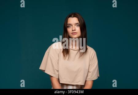 Junge brünette Frau posiert im Studio, trägt lässige Kleidung, schaut direkt in die Kamera mit natürlichem Ausdruck Stockfoto
