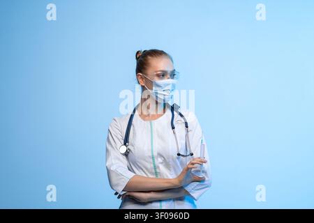 Medizinische Fachkraft im weiblichen Geschlecht, die eine Schutzmaske und eine Schutzbrille trägt und eine Spritze hält, die Impfung und Gesundheitsversorgung repräsentiert Stockfoto