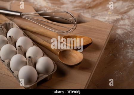 Backzutaten und Küchenutensilien auf einem Holzbrett mit verstreuter Mehl, zur Vorbereitung von Speisen Stockfoto