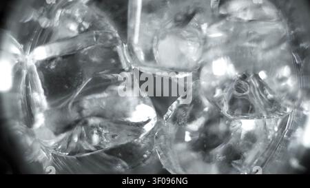 Eiswürfel füllen ein Glas mit erfrischend kaltem Wasser und erzeugen eine kühle Textur und ein abstraktes Muster in einer Graustufen-Makroaufnahme Stockfoto