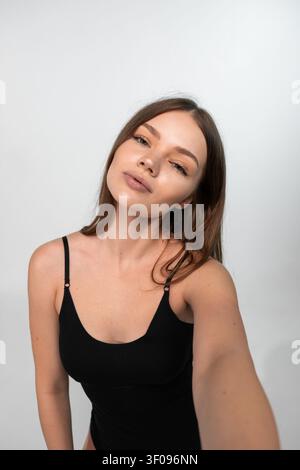 Junge Frau, die ein Selfie macht, zeigt einen selbstbewussten Ausdruck und natürliche Schönheit auf einem weißen Hintergrund Stockfoto