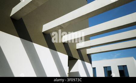 Moderne architektonische Betonträger werfen geometrische Schatten auf eine Gebäudefassade unter blauem Himmel Stockfoto