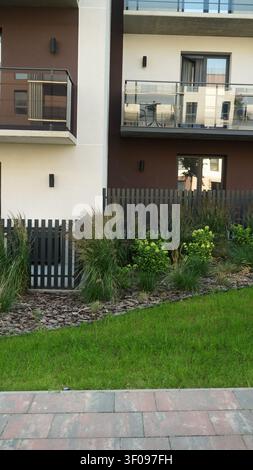 Moderne Wohnhausfassade mit zeitgenössischer Architektur, eleganten Balkonen, grünem Rasen, Gartenlandschaft Stockfoto
